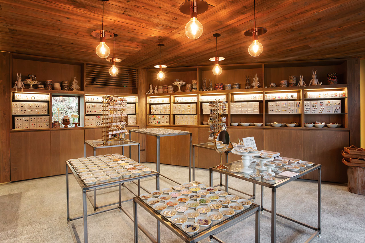 温かみある木目調の店内。壁面の照明付きケースにアクセサリーが並び、中央のテーブルに小皿が展示されている