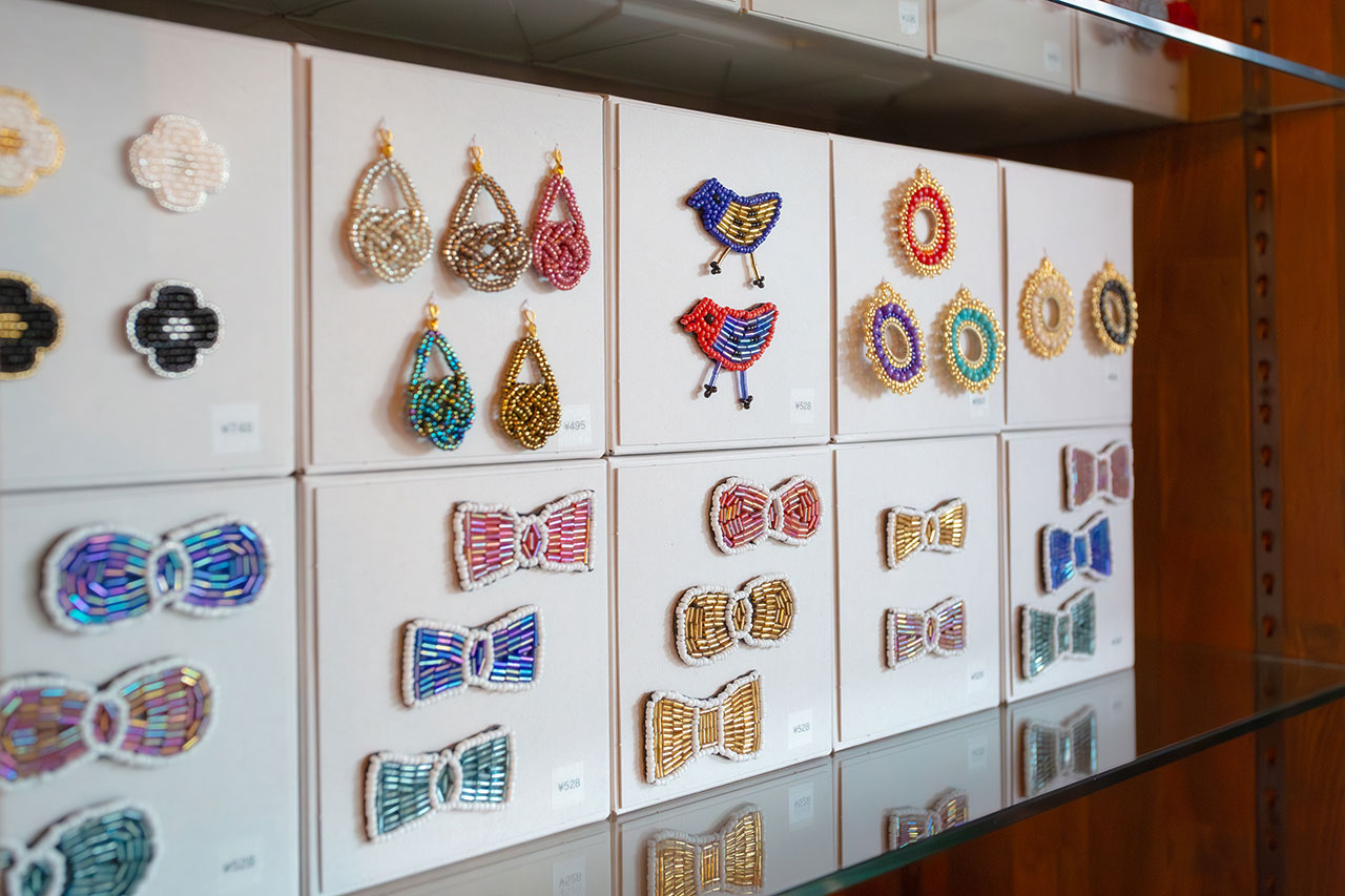 壁面ディスプレイのビーズ刺繍アクセサリー。鳥やティアドロップ、リボン型など精緻な作品